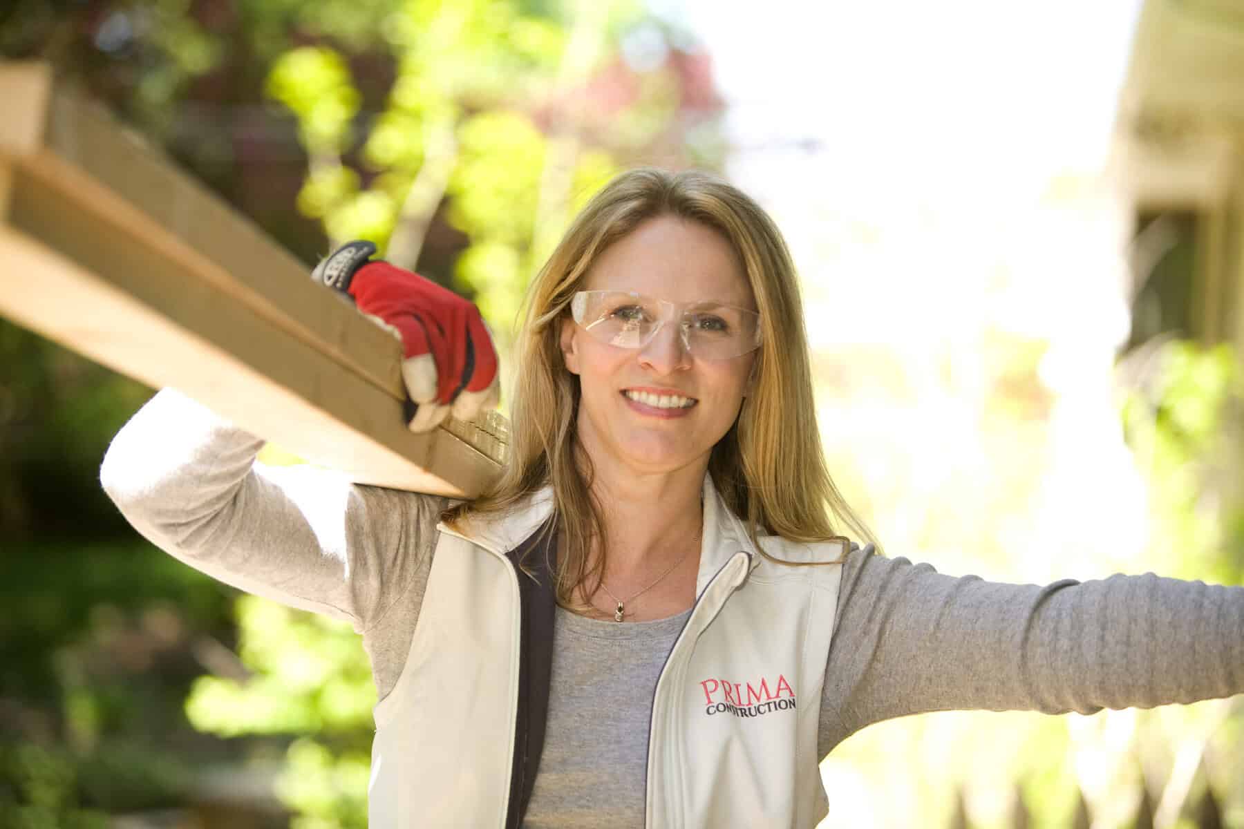 a woman wearing safety goggles and a white vest carrying a beam