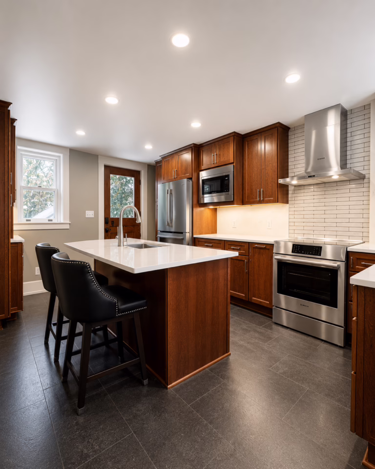 Finished kitchen with wood cabinets, island, black stools, stainless appliances.