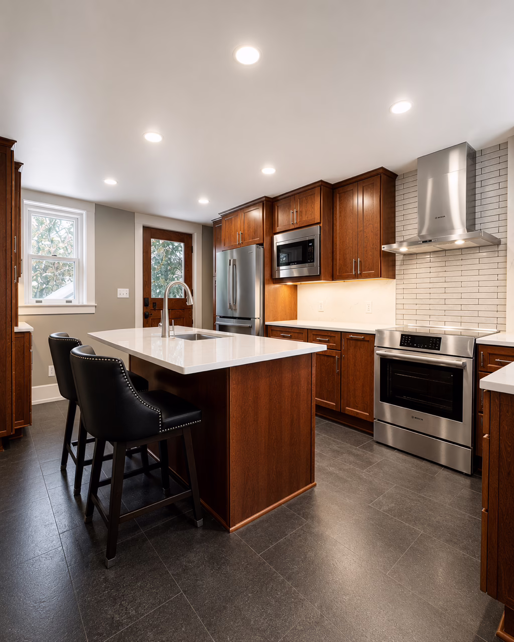 Finished kitchen with island, black stools, wood cabinets, stainless oven and hood.