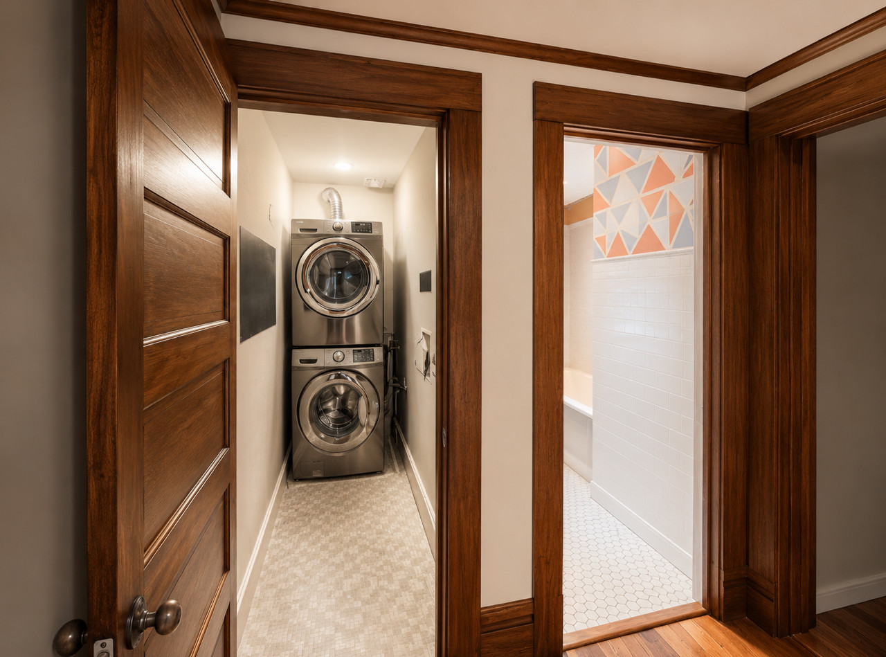 Open wood door reveals narrow laundry closet with stacked washer and dryer.