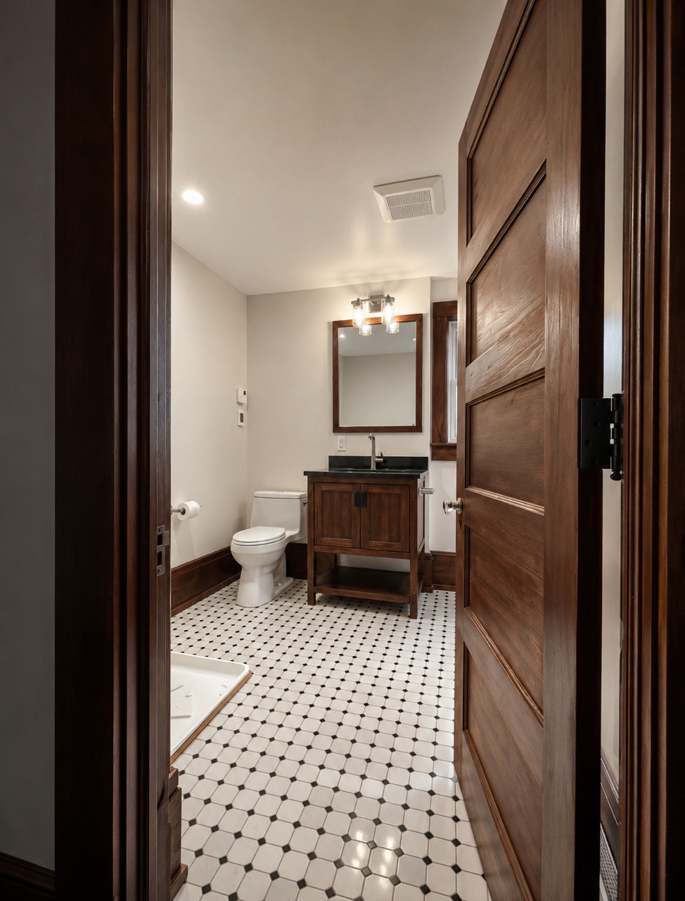 Finished bathroom with wood vanity, mirror, toilet, and black-and-white tile floor.