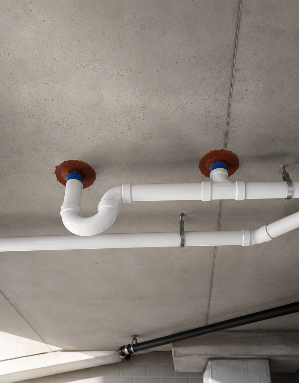 White PVC drain pipes running across a concrete ceiling with red fire collars.