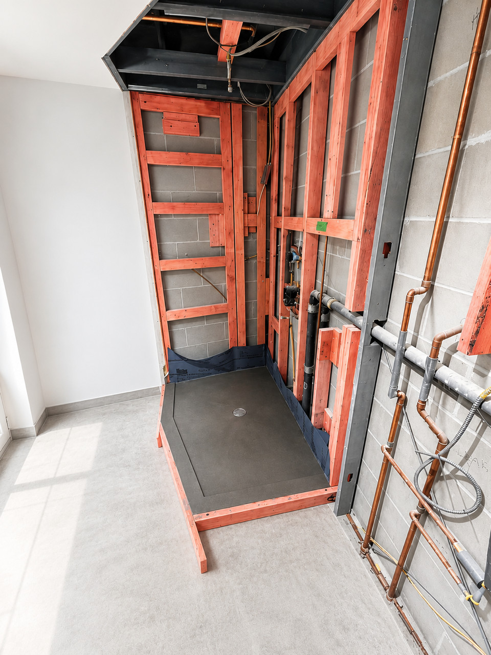 Framed shower enclosure with wood studs, waterproof membrane, drain, and exposed pipes.