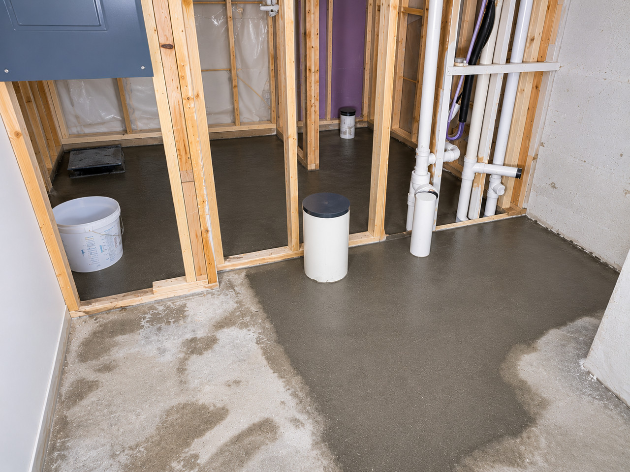 Framed basement room with freshly poured concrete floor and exposed plumbing.