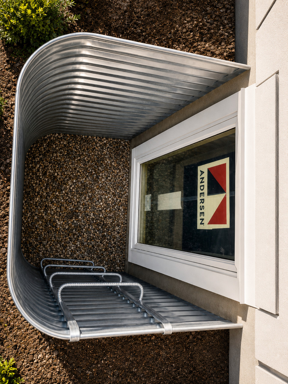 Exterior egress window with metal window well and gravel base.
