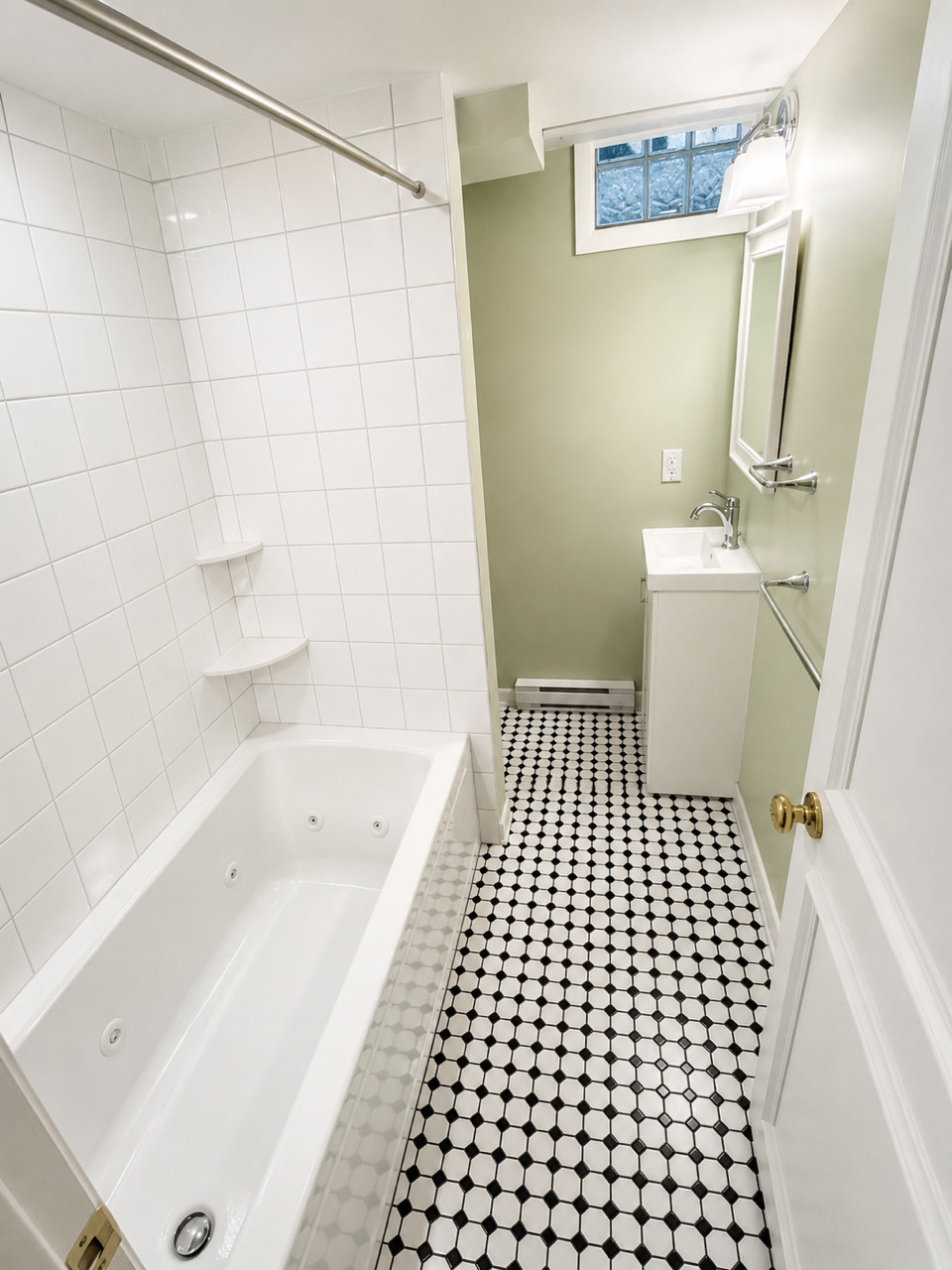 Finished bathroom with white tile tub, black-and-white floor, mint-green walls.