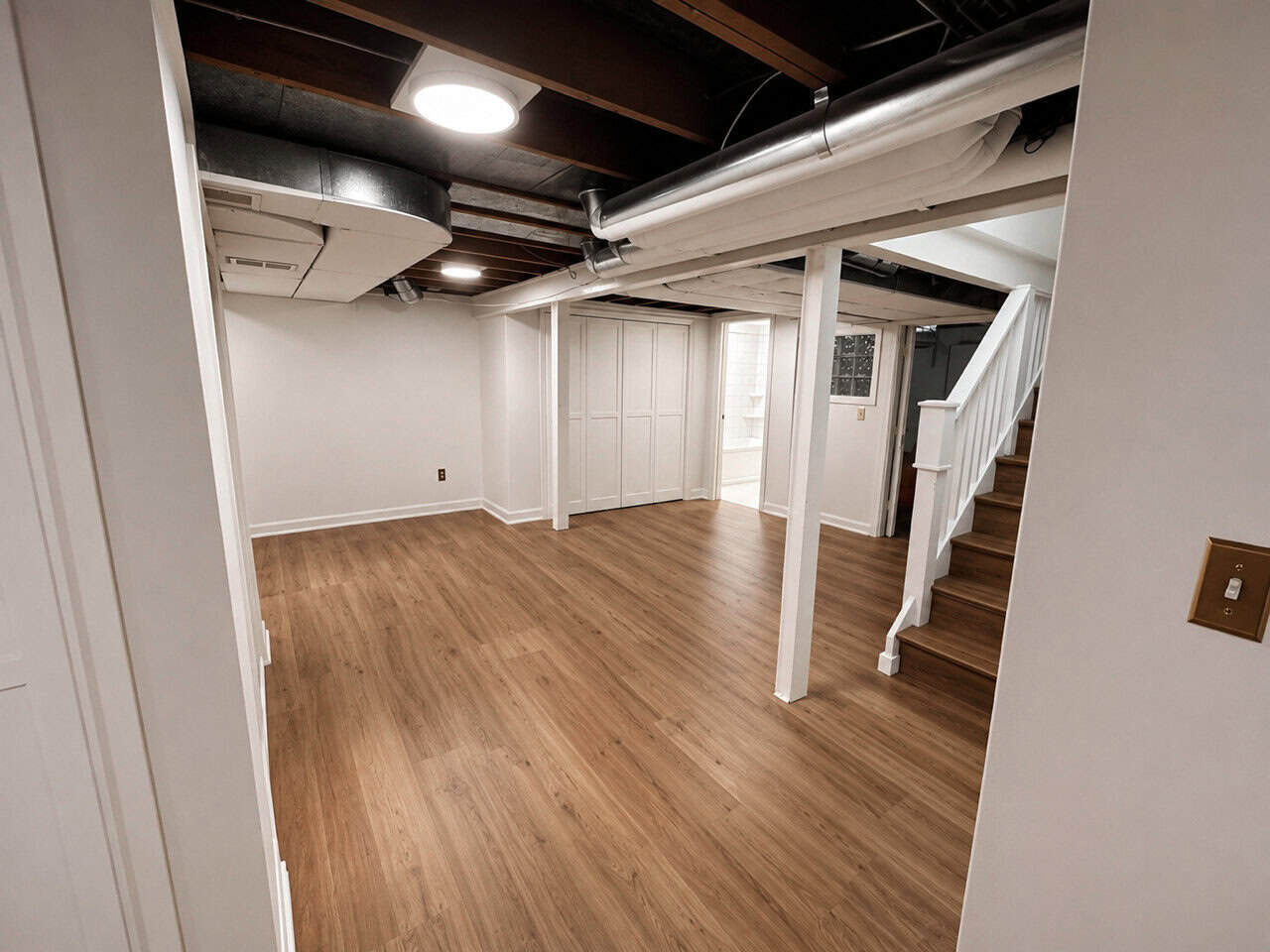 Finished basement with wood floors, white walls, recessed lighting, wood stairs.