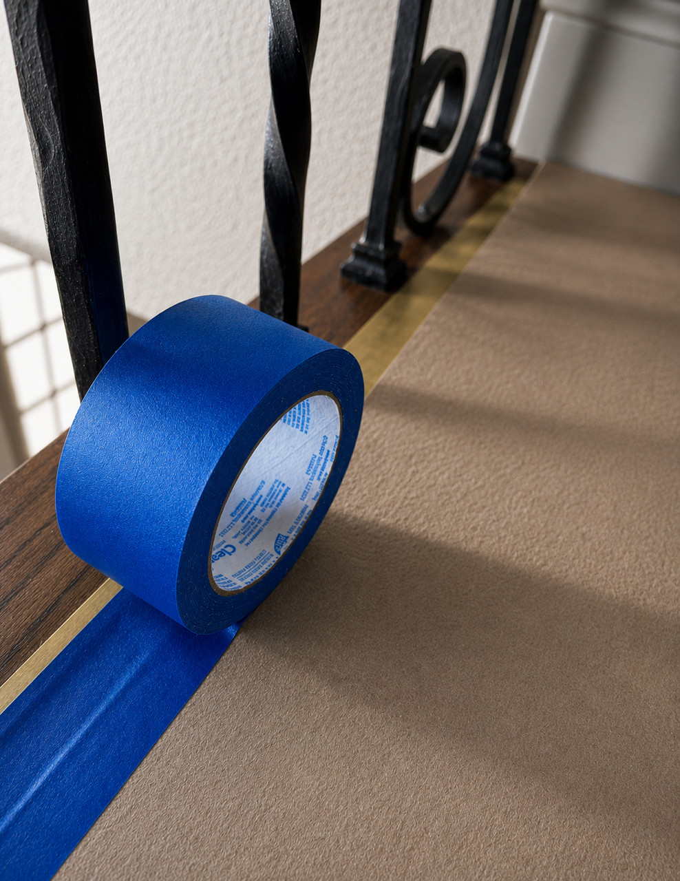 Roll of blue painter's tape on a wood handrail with paper covering.