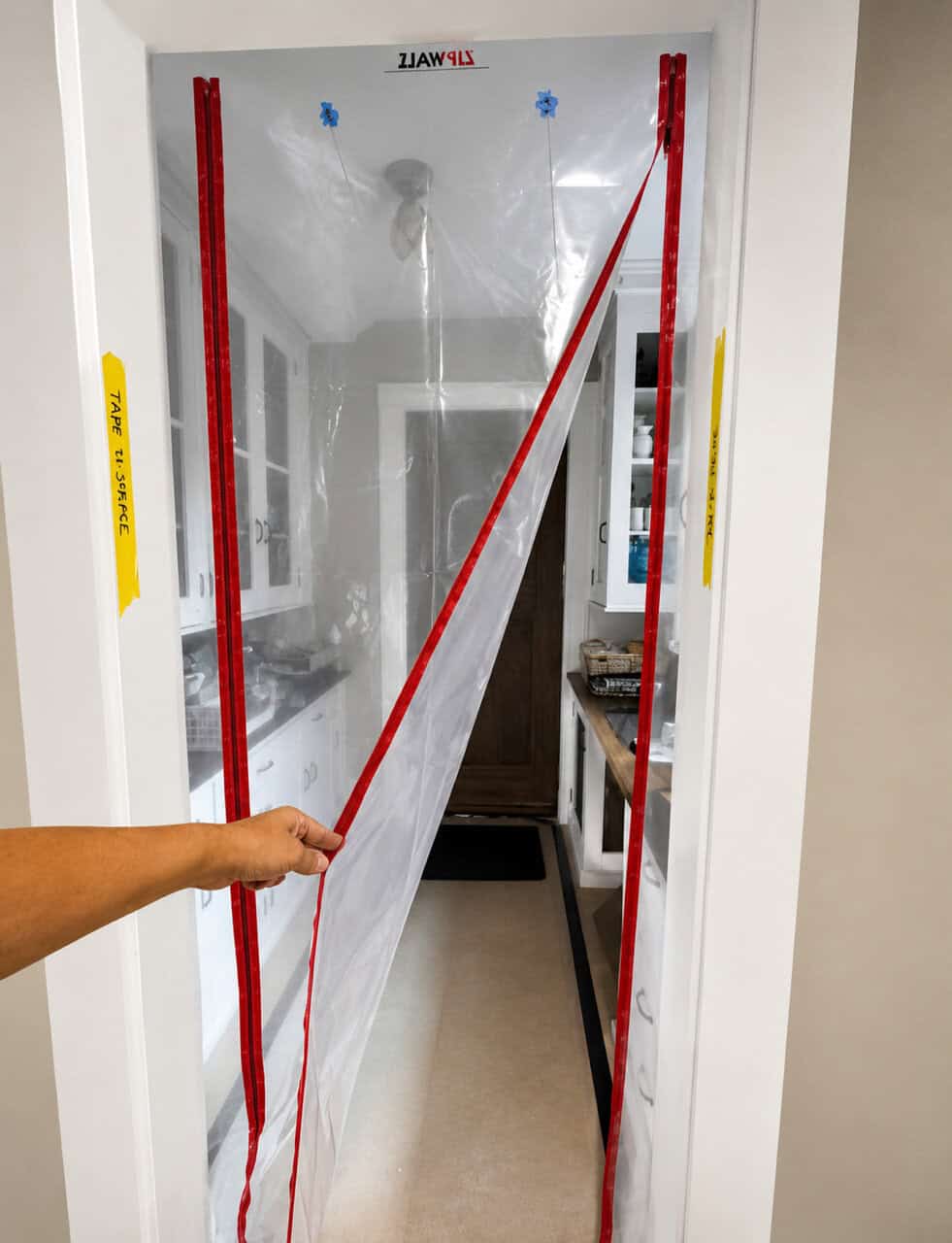 Hand unzipping a ZipWall plastic dust barrier in a doorway.