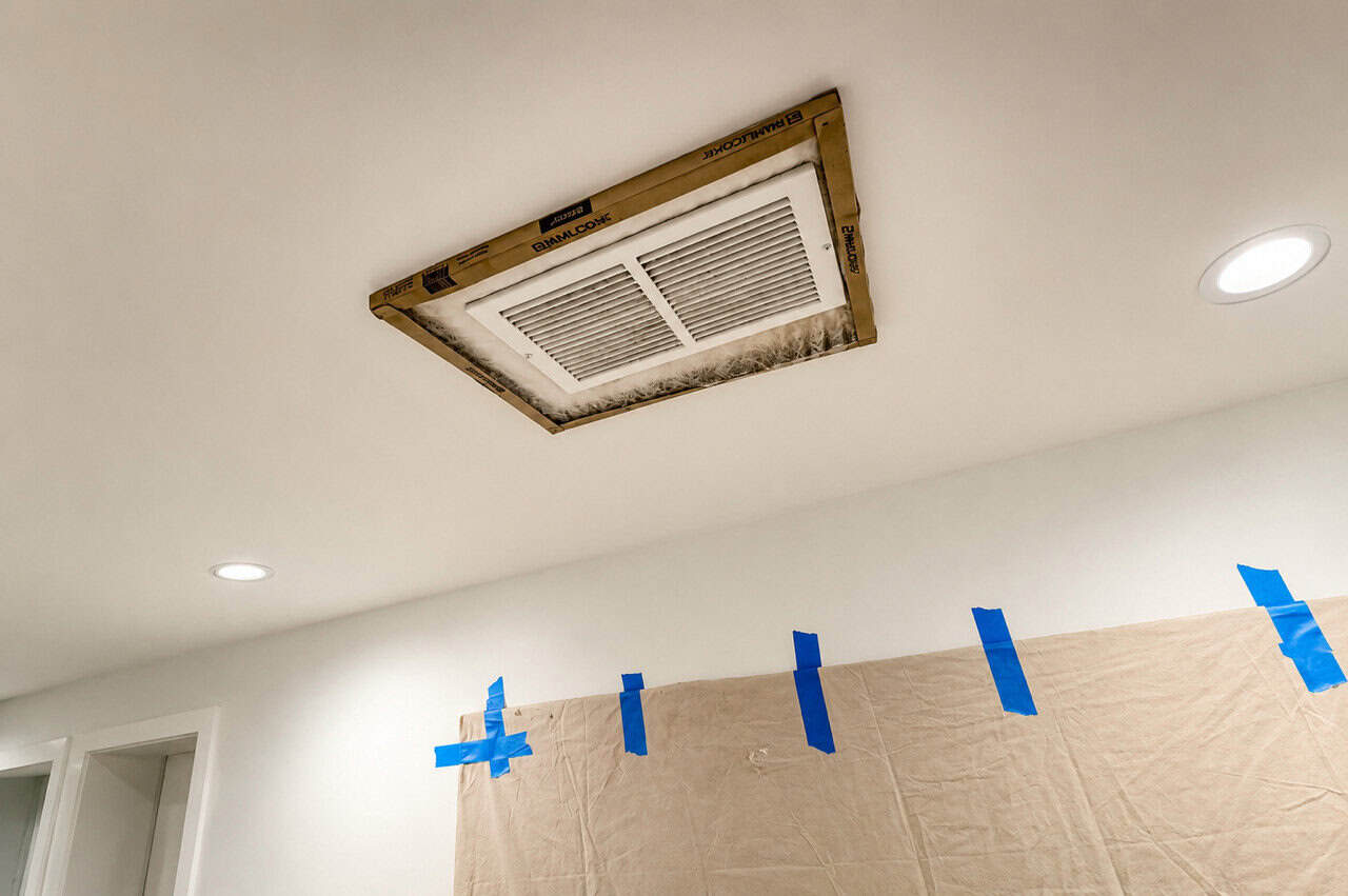 Ceiling HVAC return vent covered with filter media and taped.