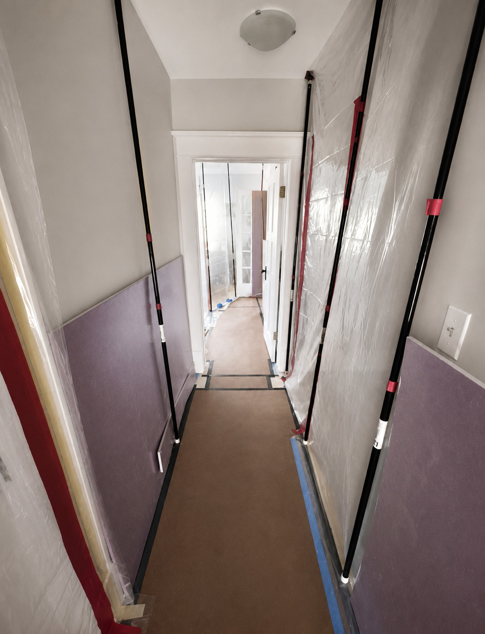 Hallway lined with plastic sheeting held by support poles, floors covered.